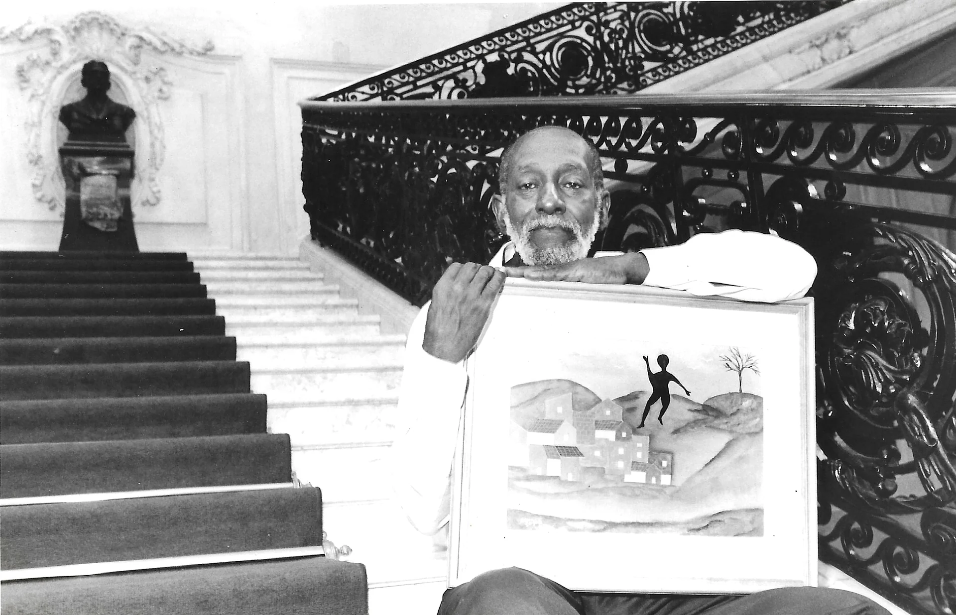 Nelson Sargento sentado junto a uma pintura de sua autoria.